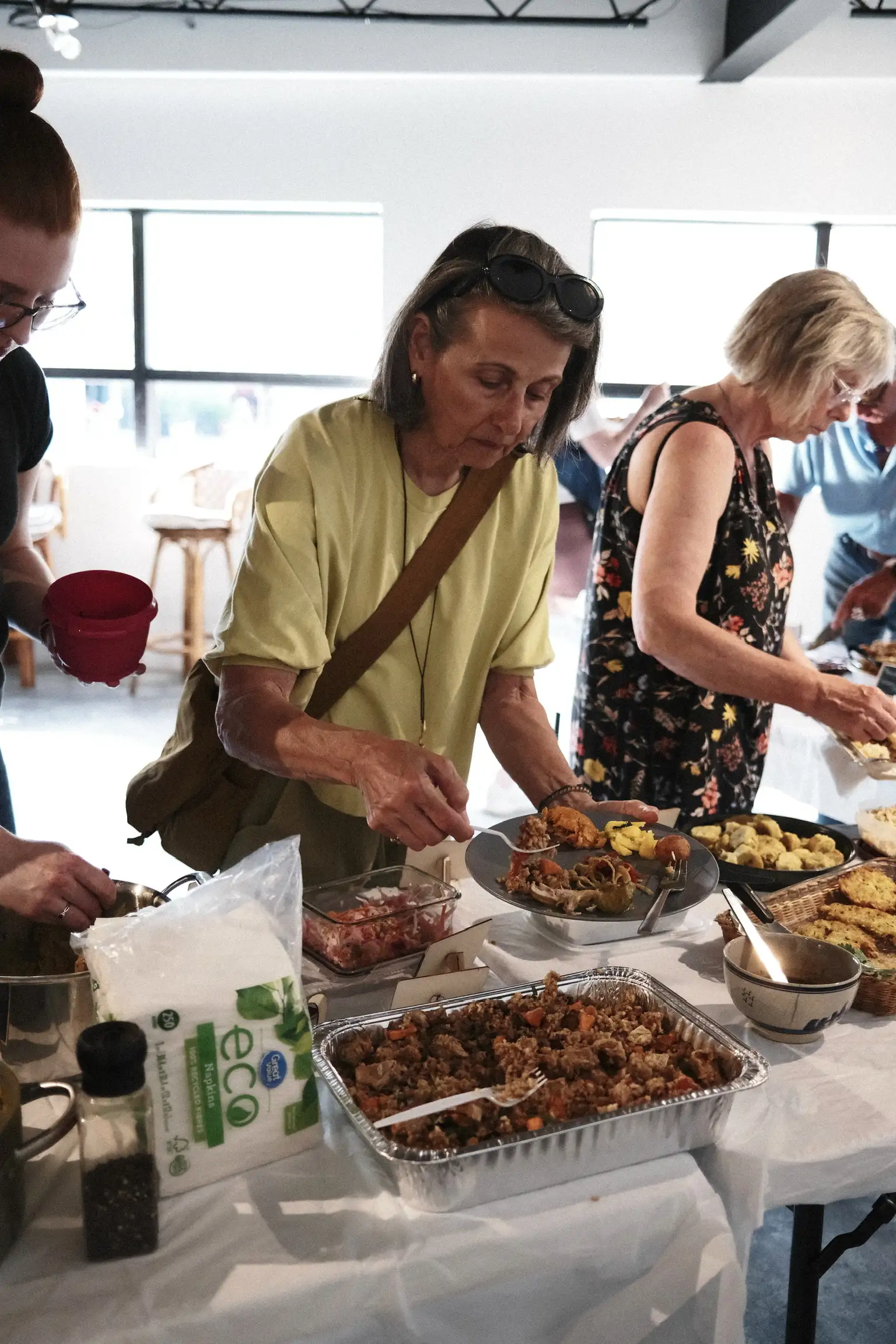 A guest serving herself from a foil tray at the Sauté Sundays table, with fritters, slaw and bread lined up alongside