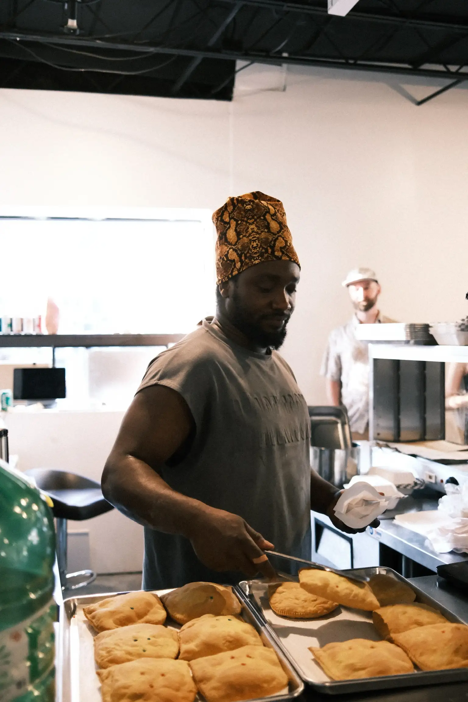 A cook in a patterned hat lifting freshly baked patties off a tray in the kitchen at Sauté Sundays