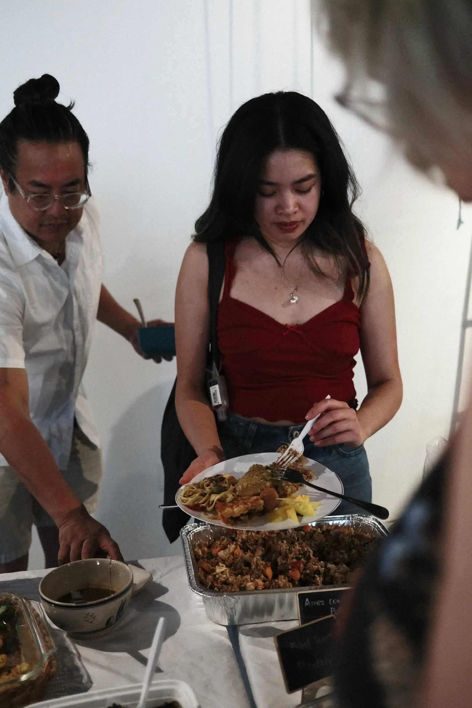 A guest holding a full plate above a tray of arroz con pollo at the Sauté Sundays table