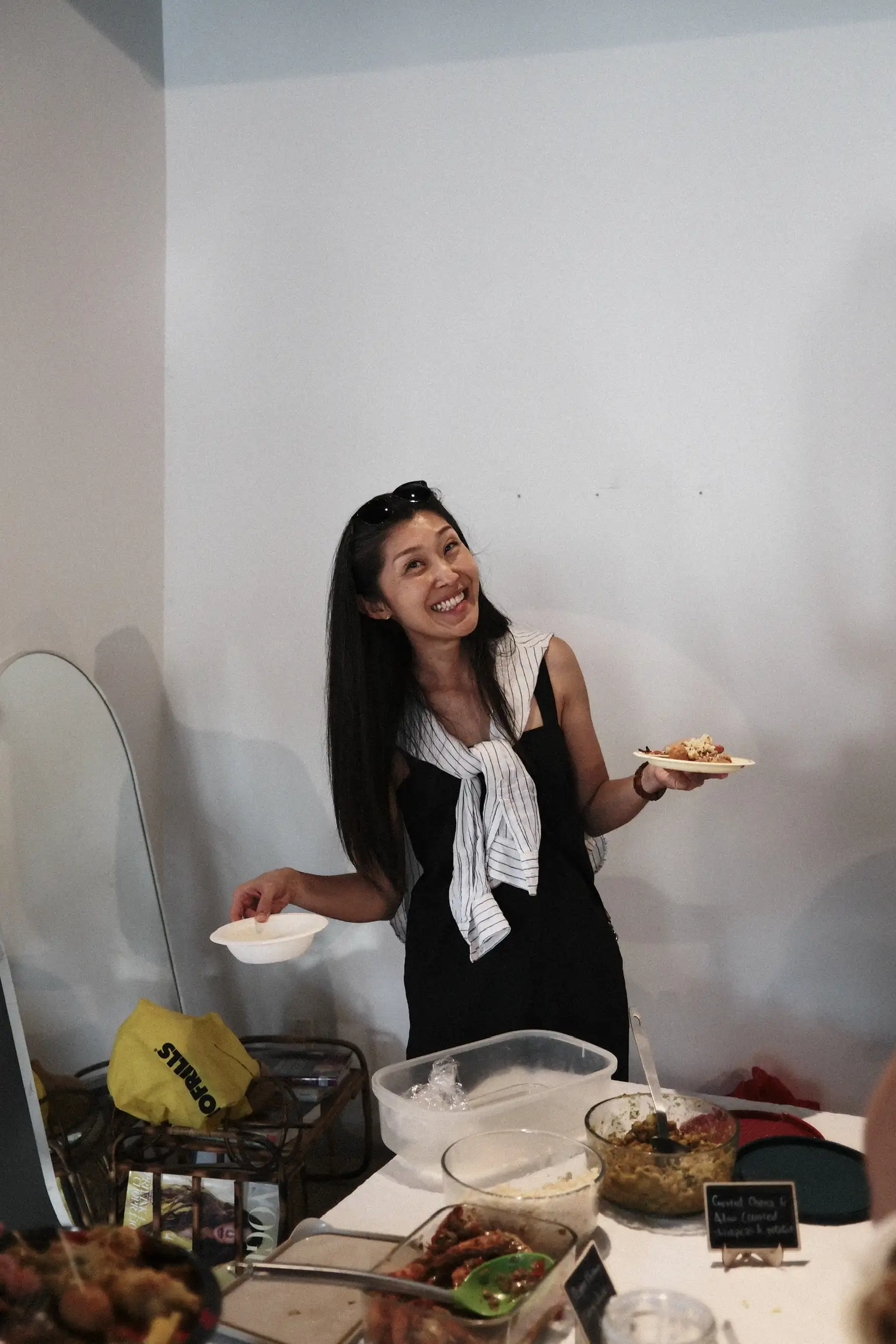 A guest laughing with a plate in one hand and a bowl in the other, next to a table of labelled dishes at Sauté Sundays
