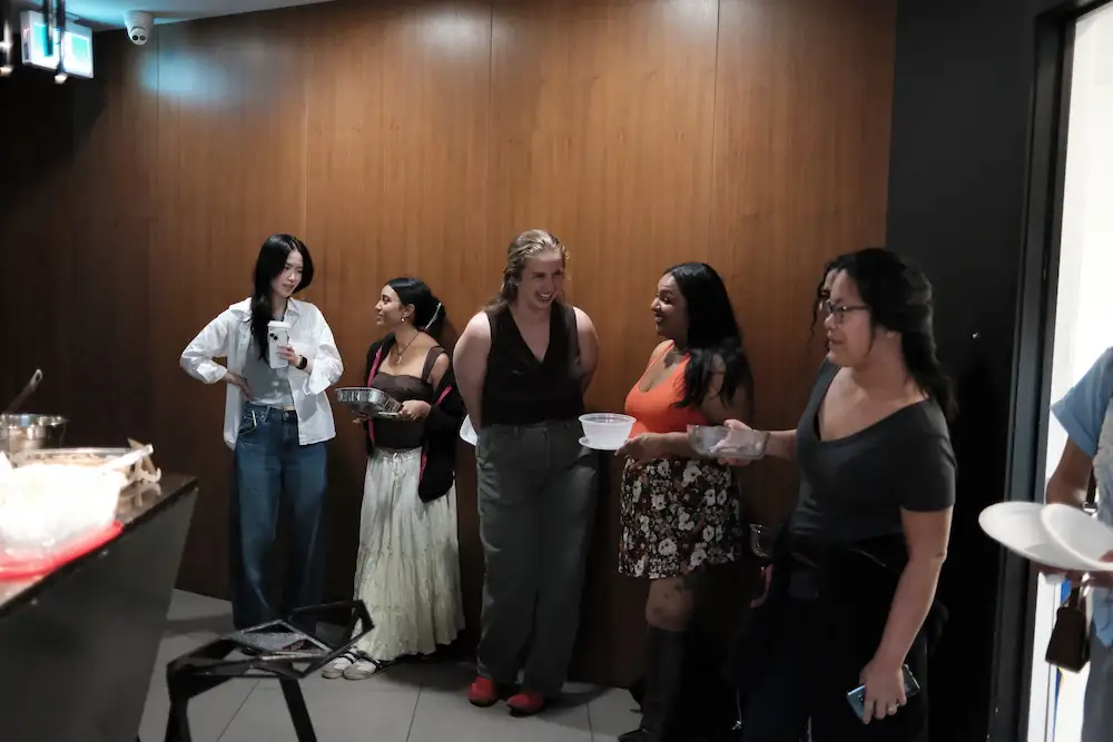 Guests standing along the wall with plates and bowls, eating and talking