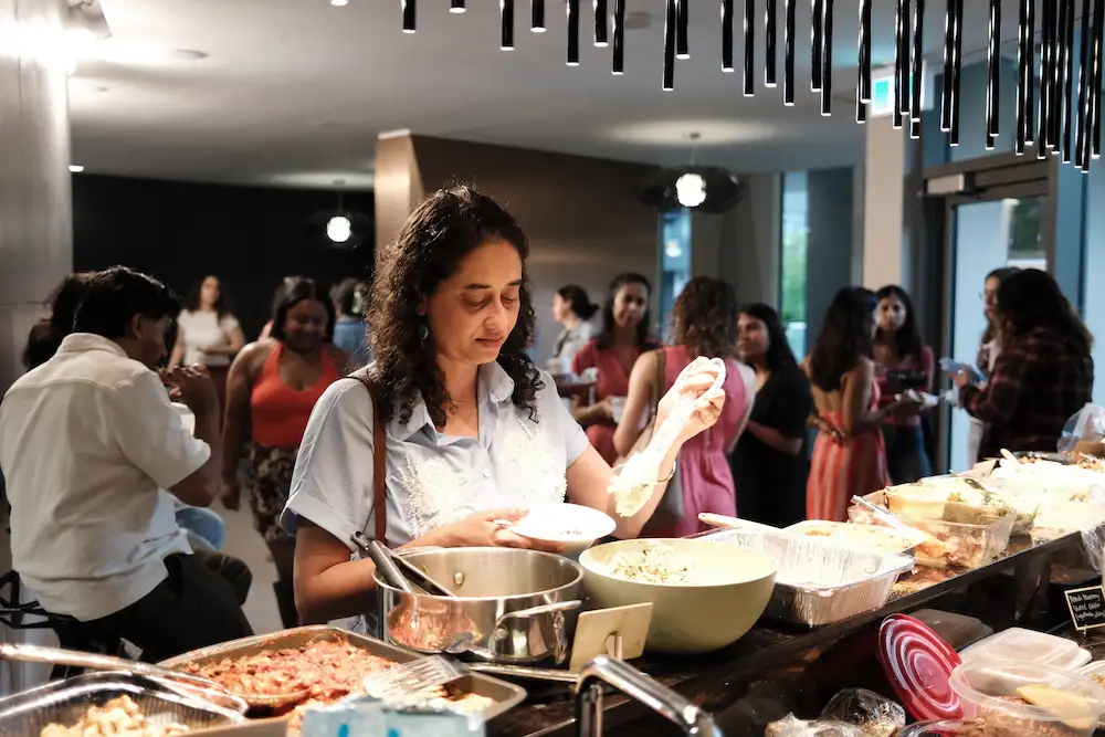 A guest spooning food onto her plate at the counter, the room busy behind her