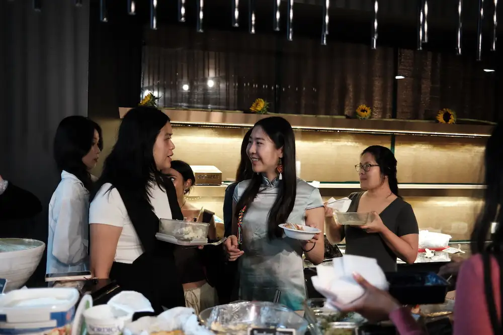Four guests standing with full plates, talking over the counter at Sauté Sundays