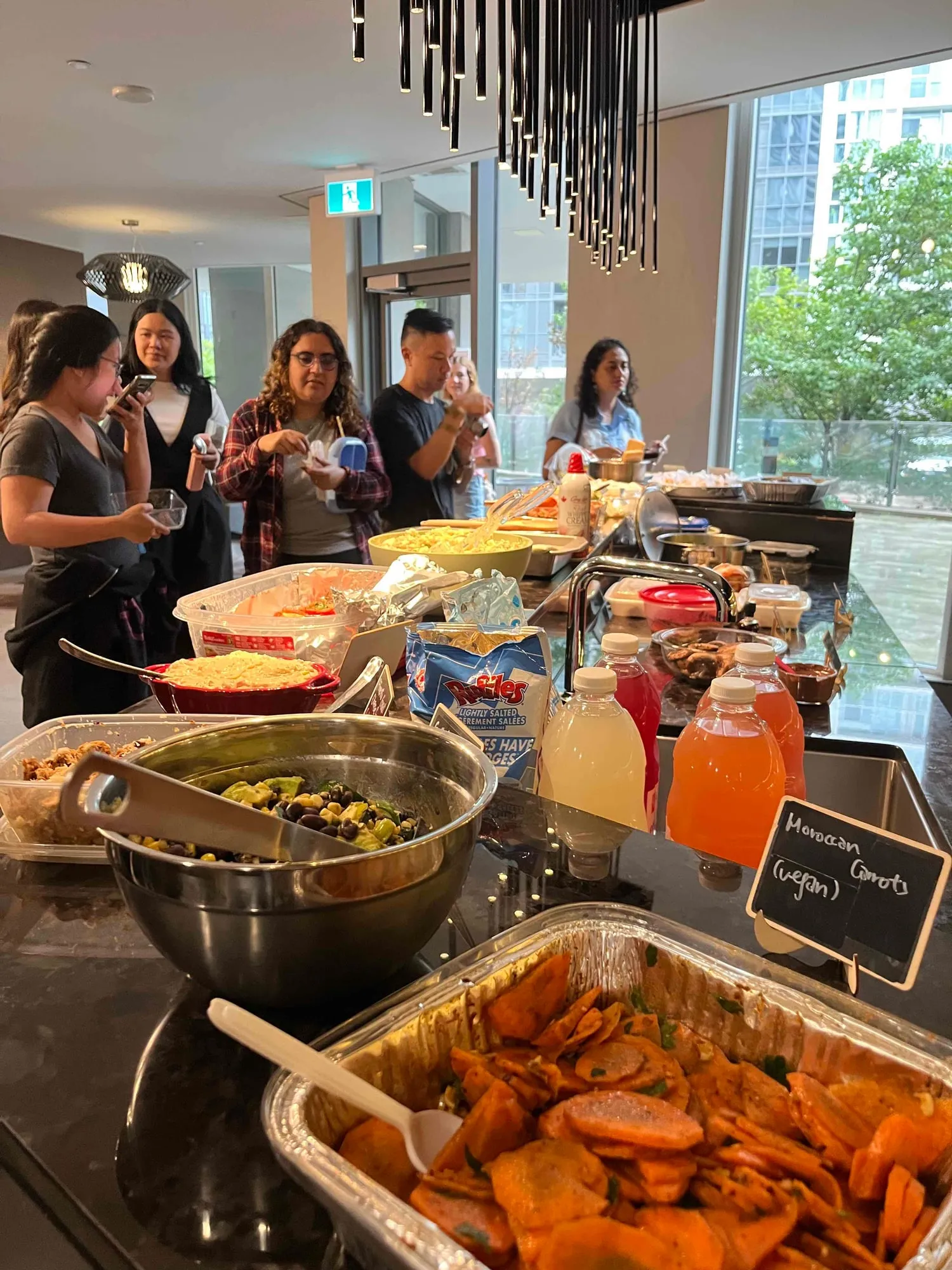 Guests filling their plates along the counter, a tray of Moroccan carrots and a bowl of black bean and corn salad in the foreground