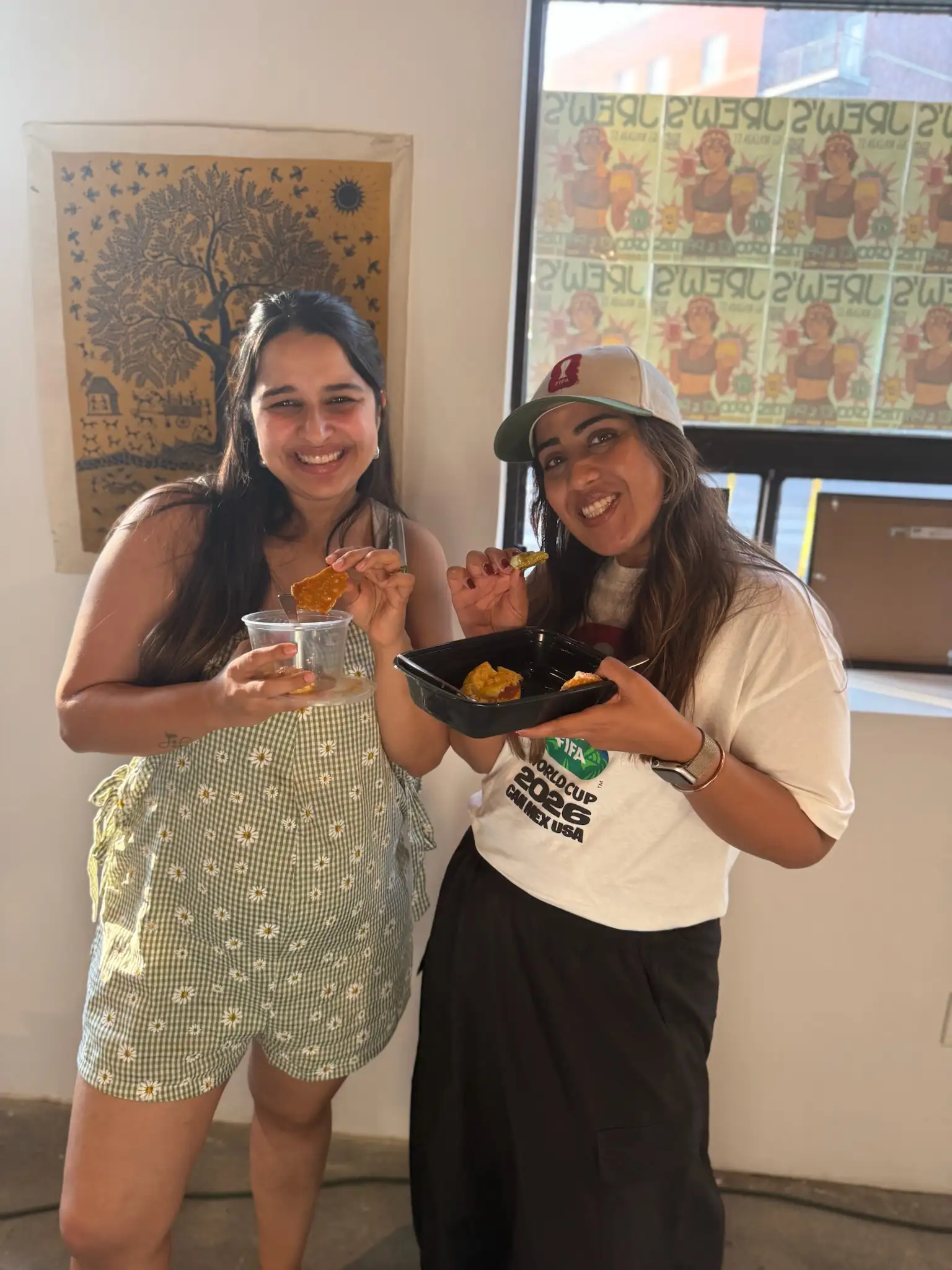 Two guests sharing a container of food in front of the Jrew's window at Sauté Sundays
