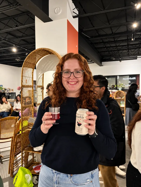 A guest smiling with a red mocktail in one hand and a can of Heartwood Sparkle in the other