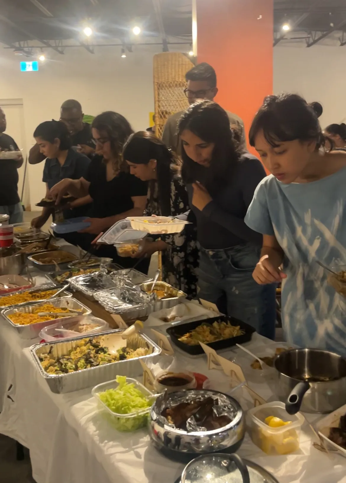Guests filling their plates along the table, foil trays and bowls spread the length of it