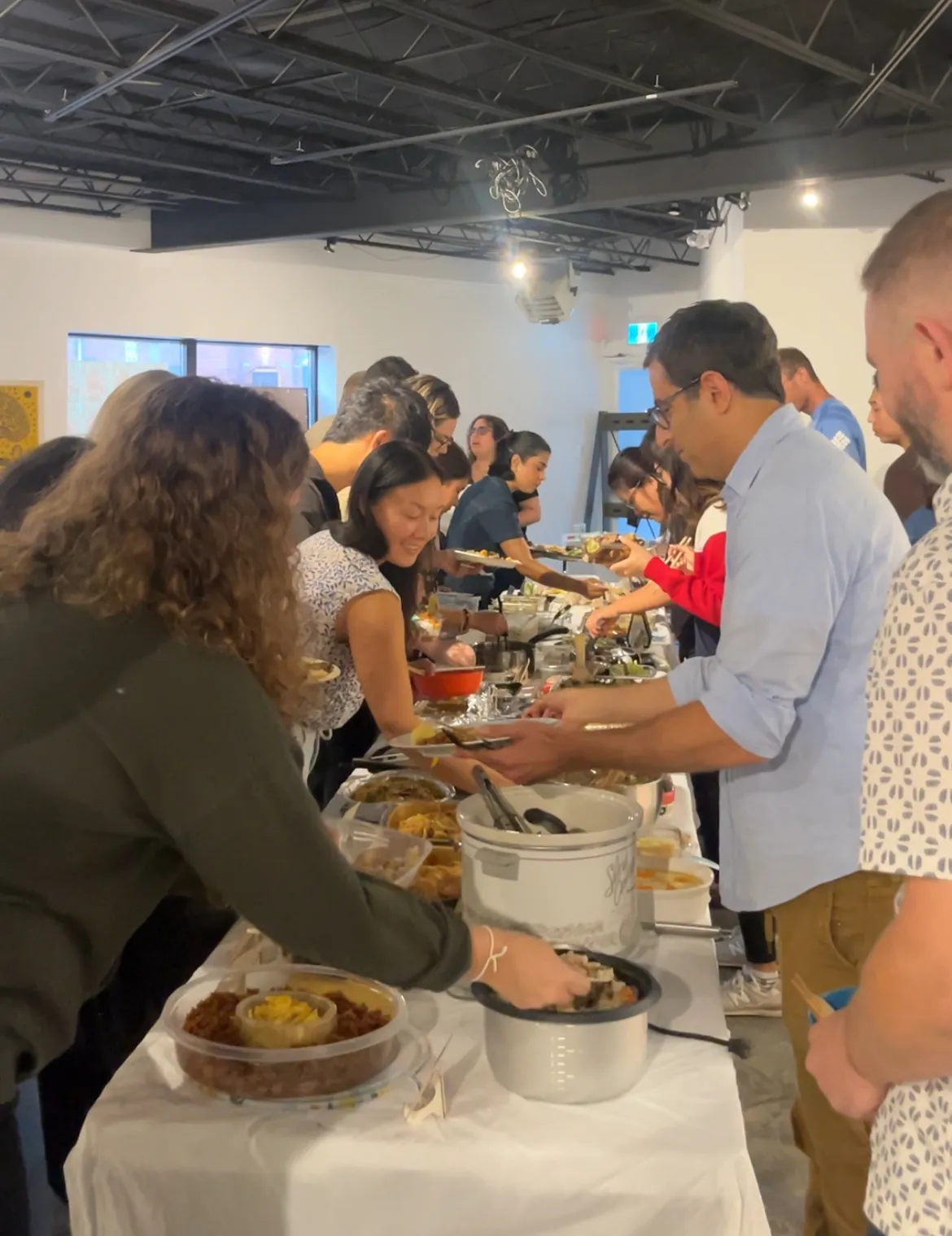 The line of guests working their way down the table, a rice cooker and a slow cooker among the dishes
