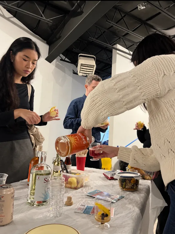Guests at the DIY mocktail bar, one pouring from a bottle of Sobrii into a glass, with bottles and glasses laid out on the table
