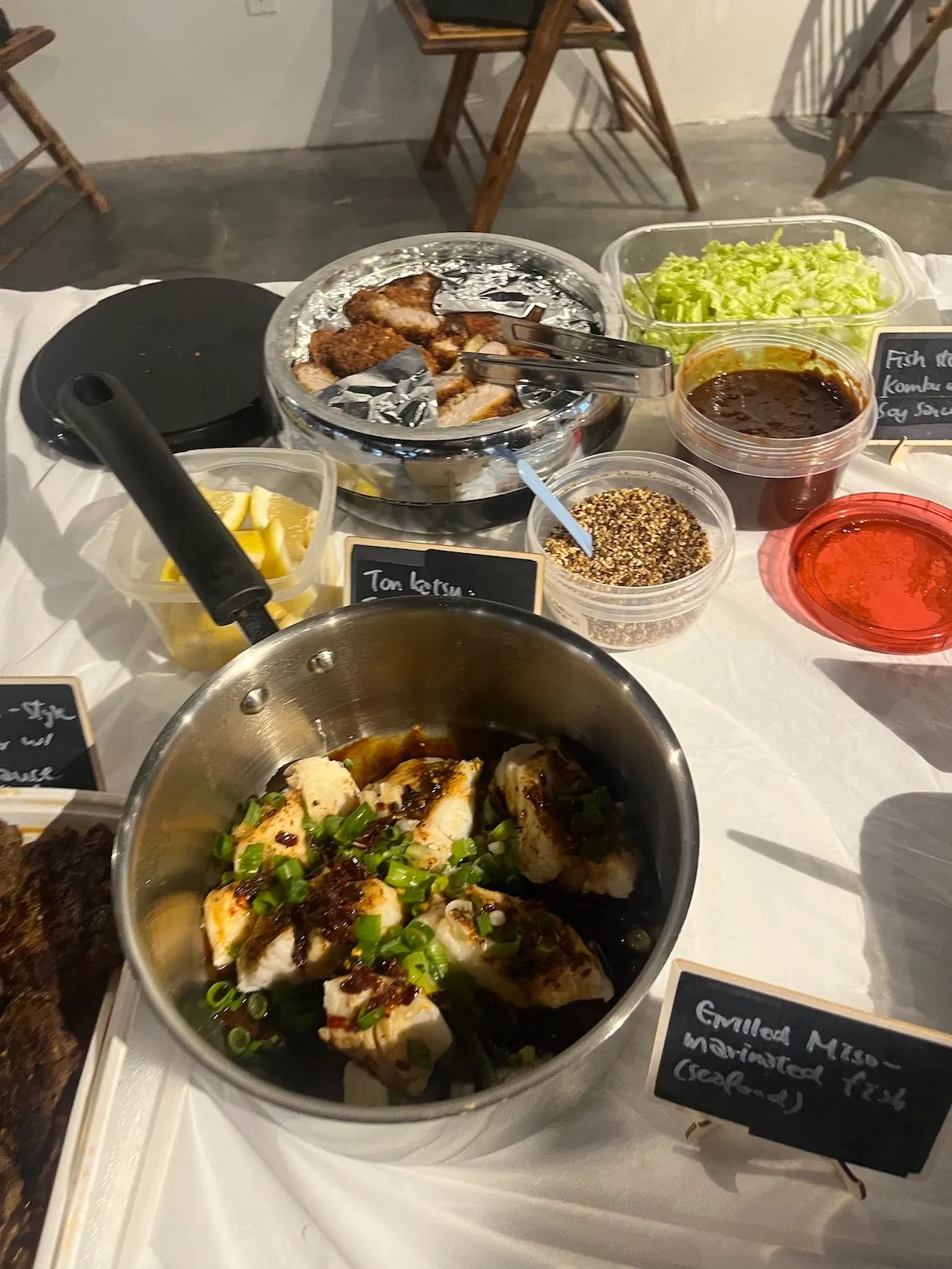 Tonkatsu and grilled miso marinated fish on the table, with lemon wedges and sesame alongside